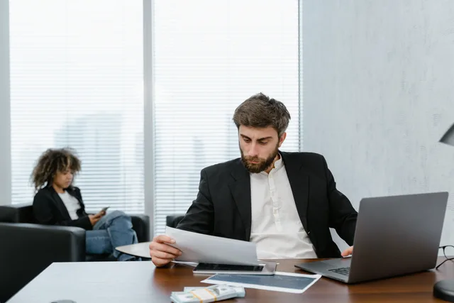 Focused businessman reviews financial reports at office desk with laptop. Costi e adempimenti dei pagamenti aziendali: carte, bonifici e incassi